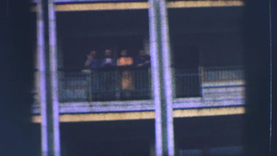 Four people remain visible on a Saint Moritz balcony, partly obscured by framing and soft 8mm exposure.