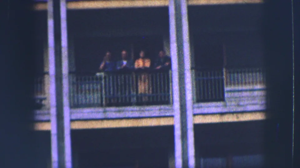 A group of four stands at a railing on a multi-story Saint Moritz building, captured in soft 1963 8mm color.