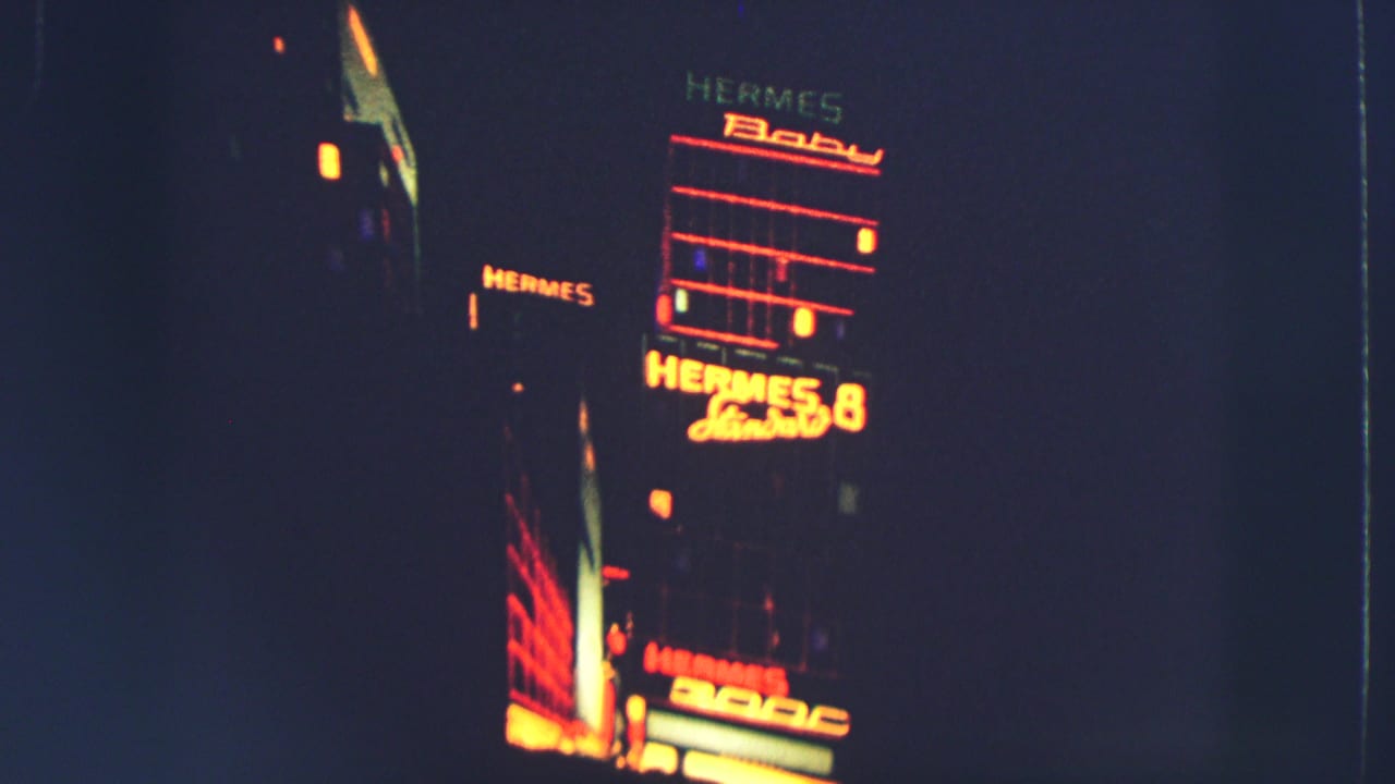 Illuminated Hermes signs on a dark building at night, framed toward the upper facade.