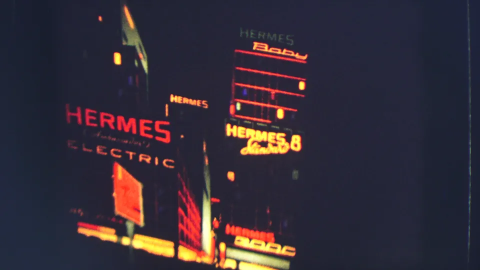 1963 Zurich 8mm frame showing multiple red-orange Hermes signs on a dark urban facade, with handheld low-light softness.