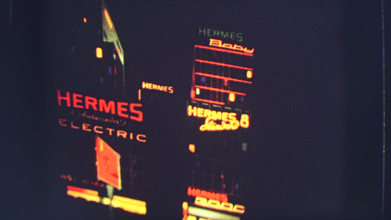 1963 Switzerland home-movie frame showing bright HERMES and ELECTRIC neon signage on a dark nighttime facade.
