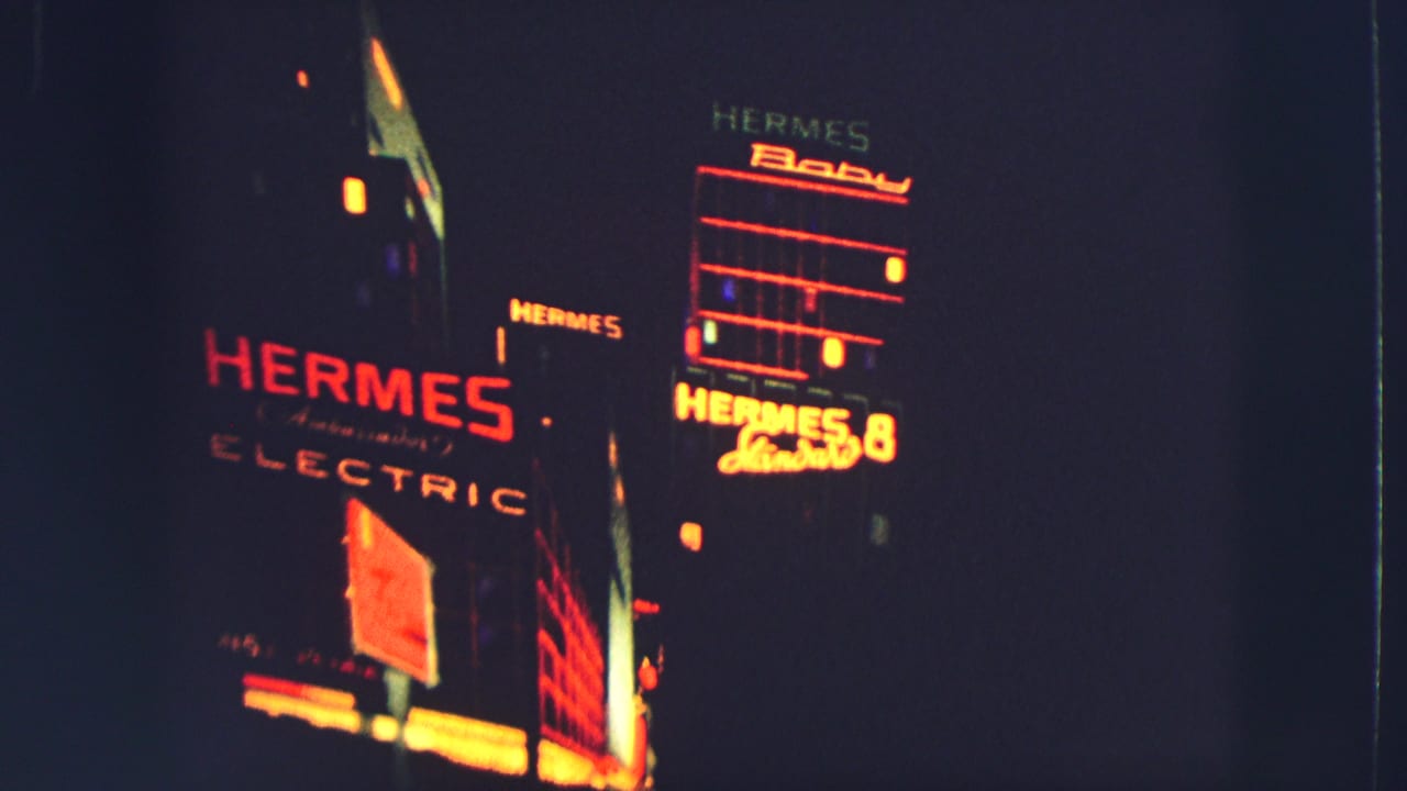 Illuminated HERMES and ELECTRIC signs appear on a dark nighttime facade.