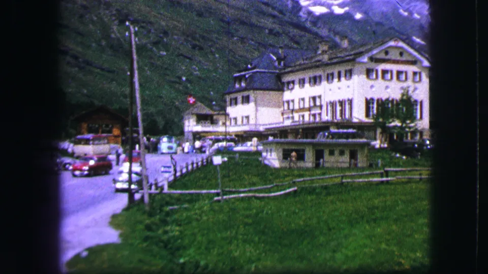 Daylight 1963 Swiss travel frame showing a white alpine hotel or resort building with lawn, cars, fencing, and mountain backdrop.