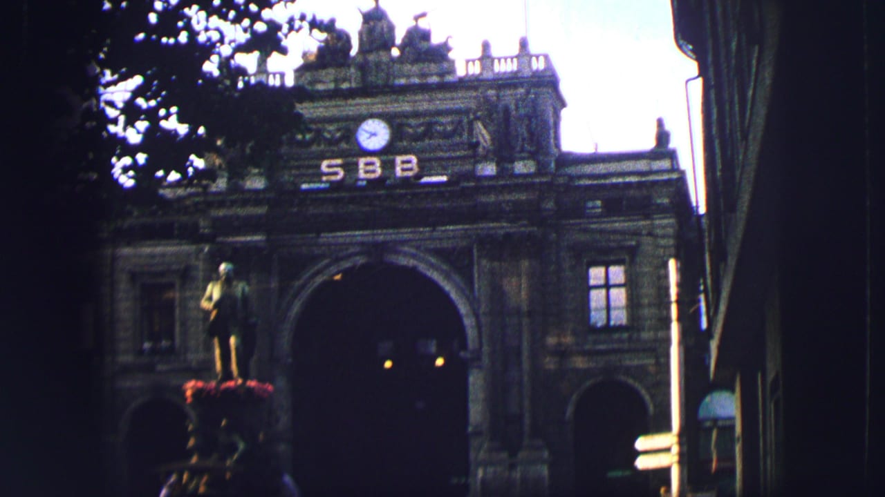 Stone arched facade with clock, SBB lettering, and a statue in the foreground.
