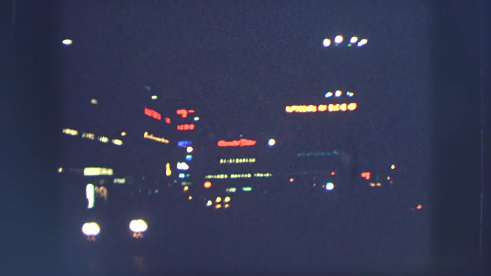 1963 Zurich night street view with soft car headlights, illuminated signs, and deep blue shadows on 8mm film.