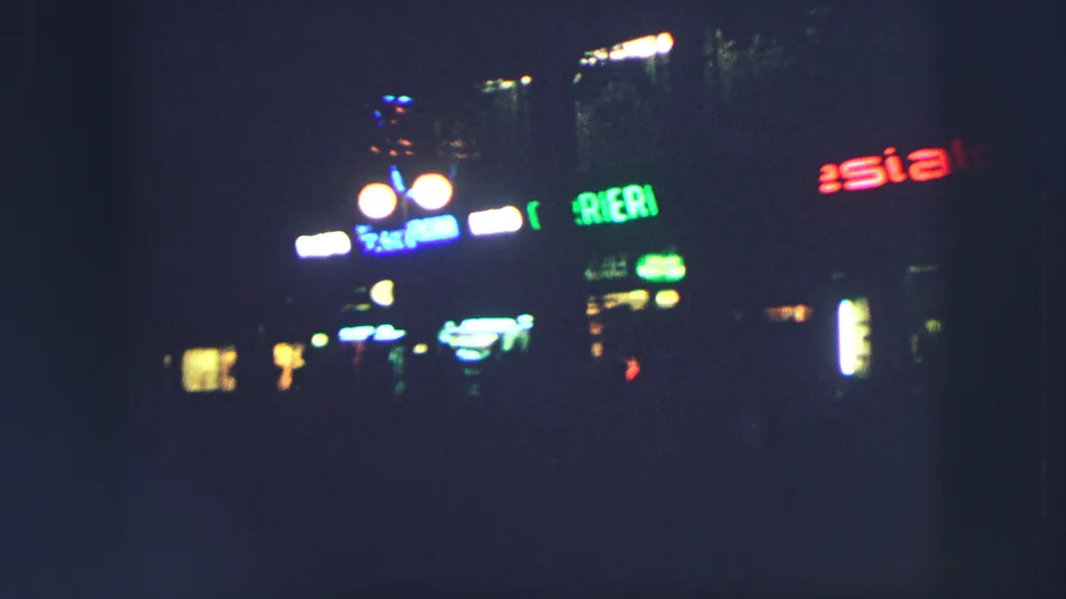 Zurich at night in 1963, with bright lamps and colored signs softened by handheld 8mm exposure.