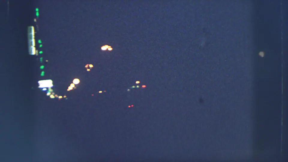A very dark 1963 Zurich night frame shows scattered street lights and faint illuminated signs on 8mm film.