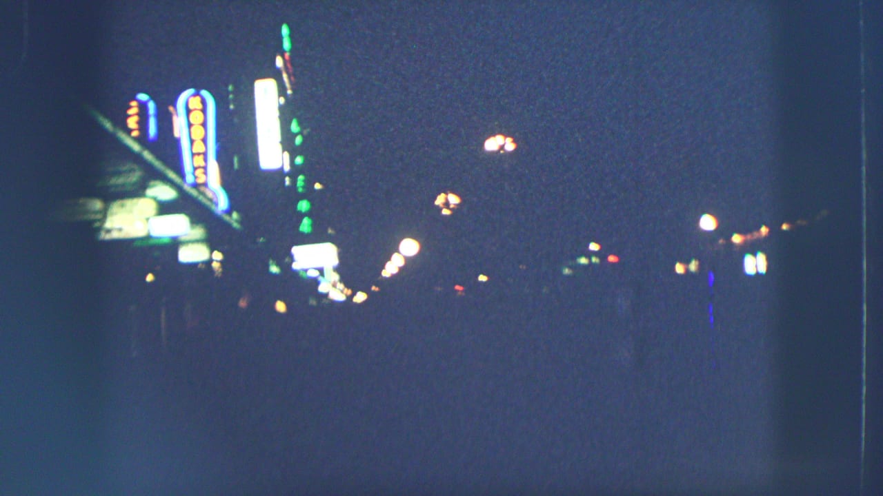1963 Zurich night street view with glowing neon signs, streetlights, and deep shadows in soft 8mm color footage.