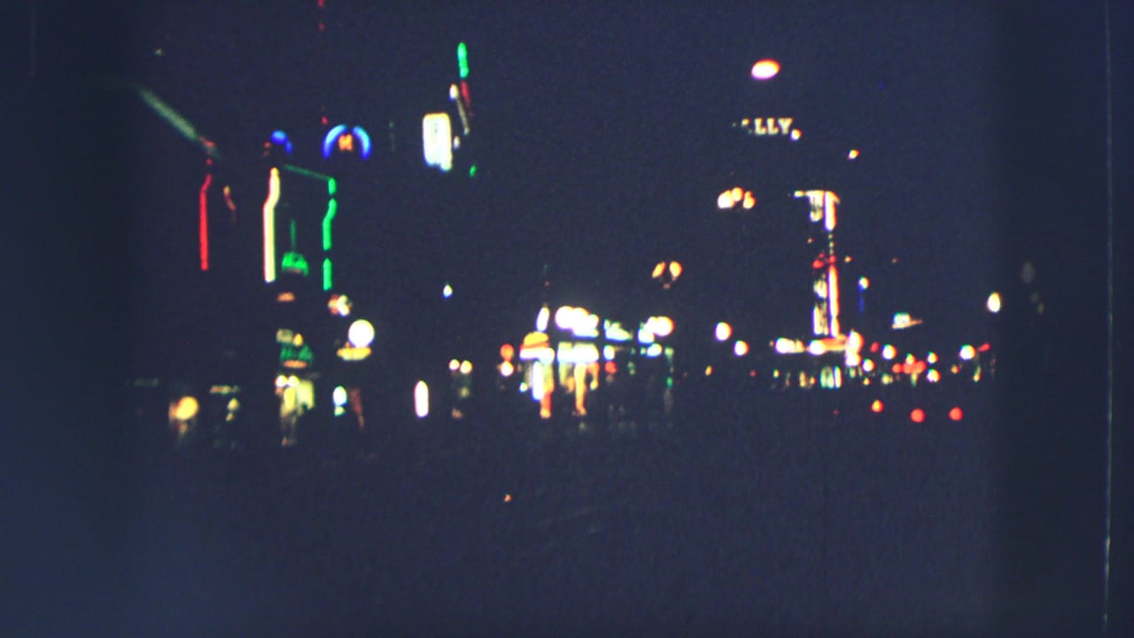 Night street with bright signs, streetlights, and distant vehicle lights.