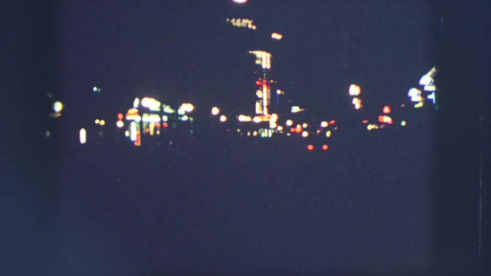 Zurich nighttime street view from 1963, showing glowing signs and streetlamps softened by grainy 8mm exposure.