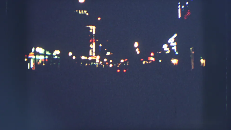 1963 Zurich city night frame with illuminated street signs, streetlights, and distant red lights against a dark roadway.