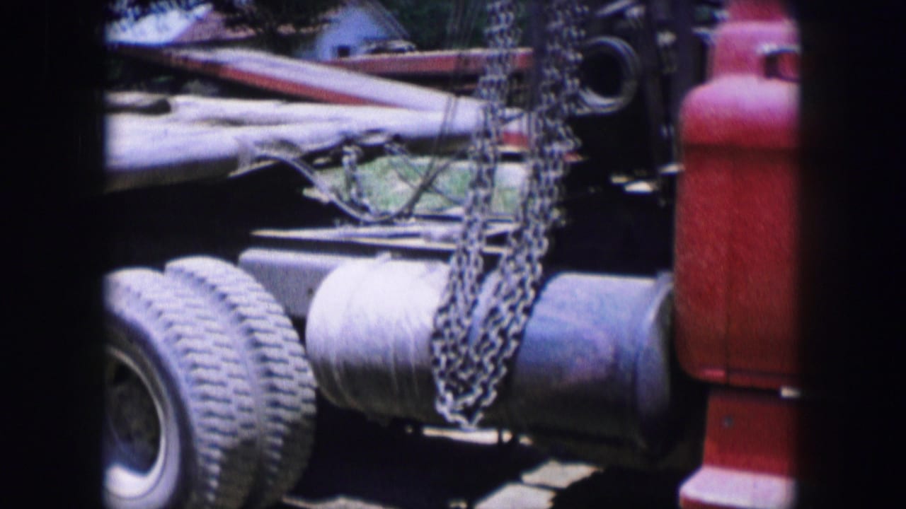 1964 Dallas 8mm frame showing a red truck side with metal chains, a rear tire, cylindrical tank, and dark film-frame bars.