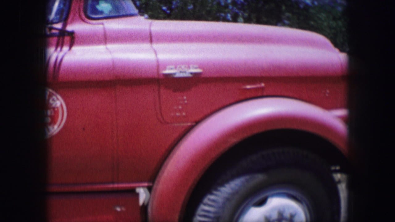 1964 Dallas-area 8mm frame showing a red vintage truck side, rounded front fender, black tire, chrome detail, and partial cab.