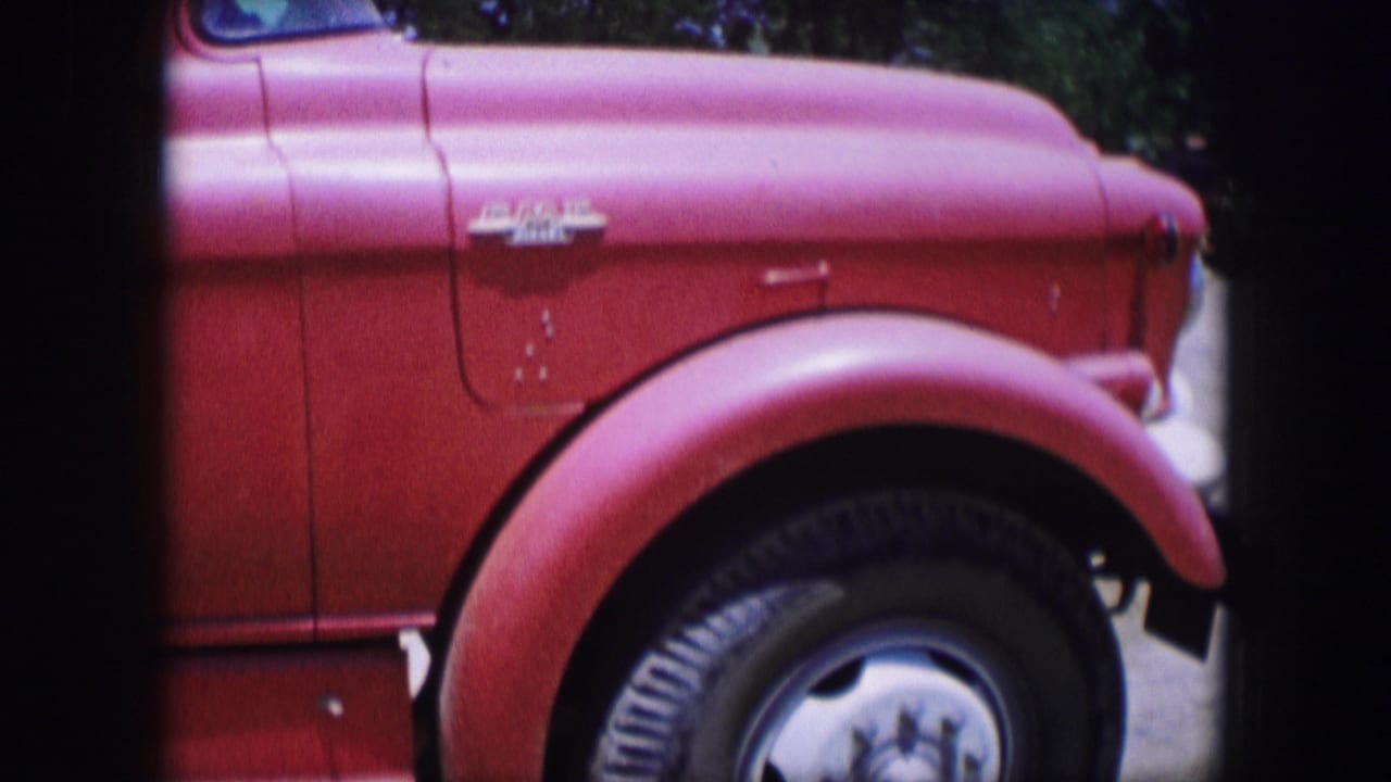Red truck front side with rounded fender, black tire, chrome trim, and partial cab in sunlight.