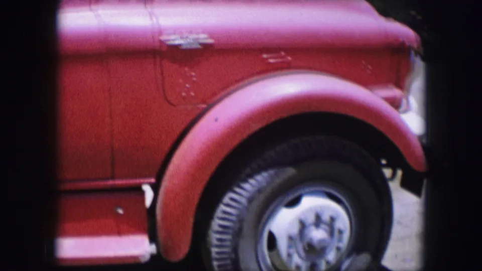 A tight 1964 8mm crop shows the red truck's front fender, black tire, chrome wheel, and small body details in bright light.