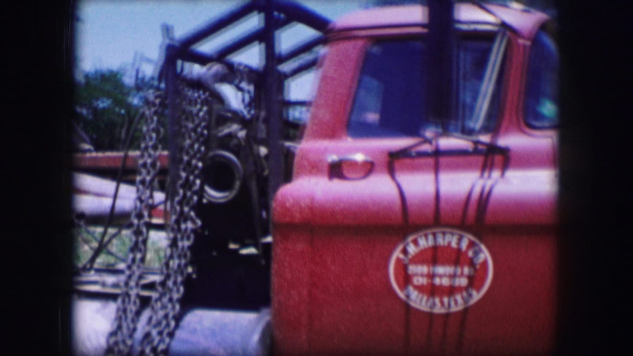 Red truck cab beside hanging chains and rear equipment.