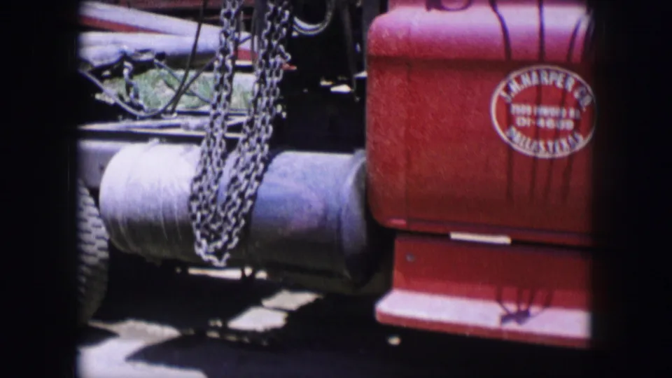 Partial view of the red utility truck in Dallas, Texas, 1964, showing chains, a tank or cylindrical part, and the door logo.