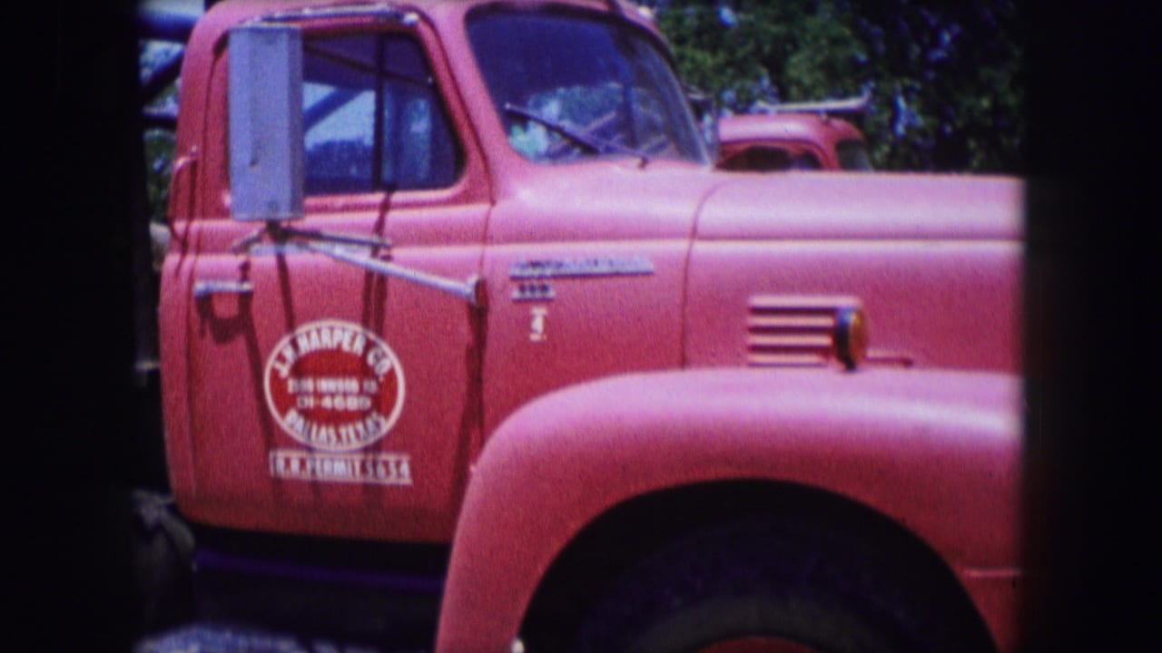 1964 Dallas 8mm frame showing a red industrial truck cab with a visible company door logo, chrome mirror, side vent, and greenery behind it.