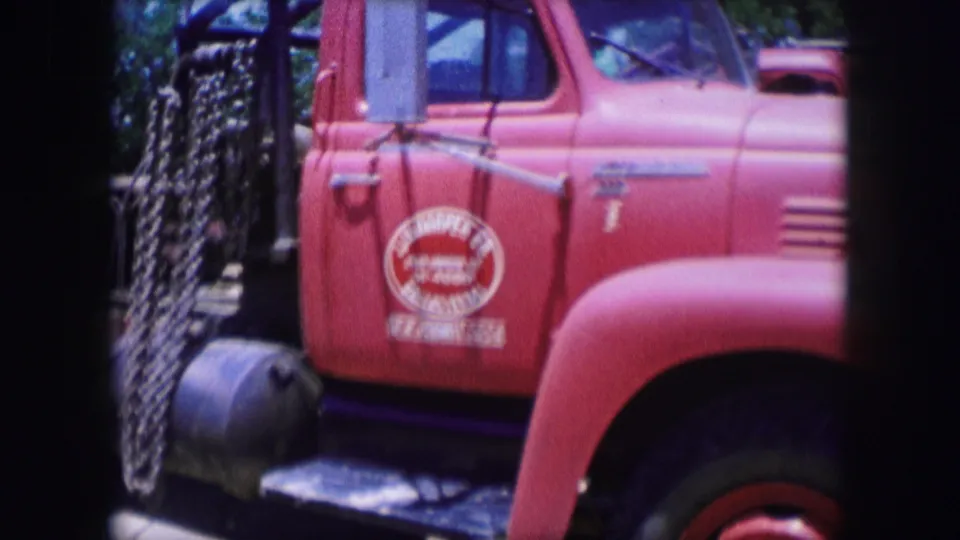 1964 Dallas frame with the red industrial truck close to camera, showing the company door logo, chrome mirror, hood, side vent, and dark structural elements.
