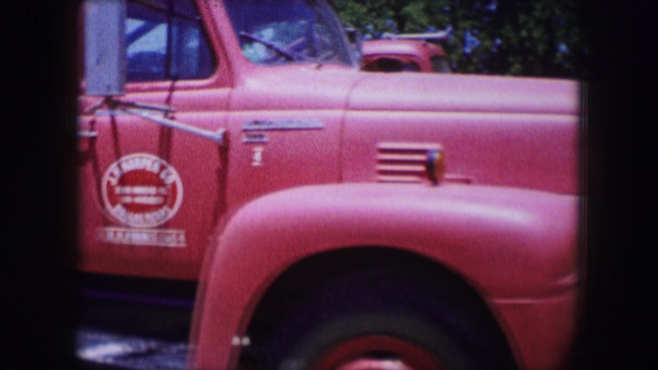 Close view of a red vintage work truck with rounded fender and painted door lettering.