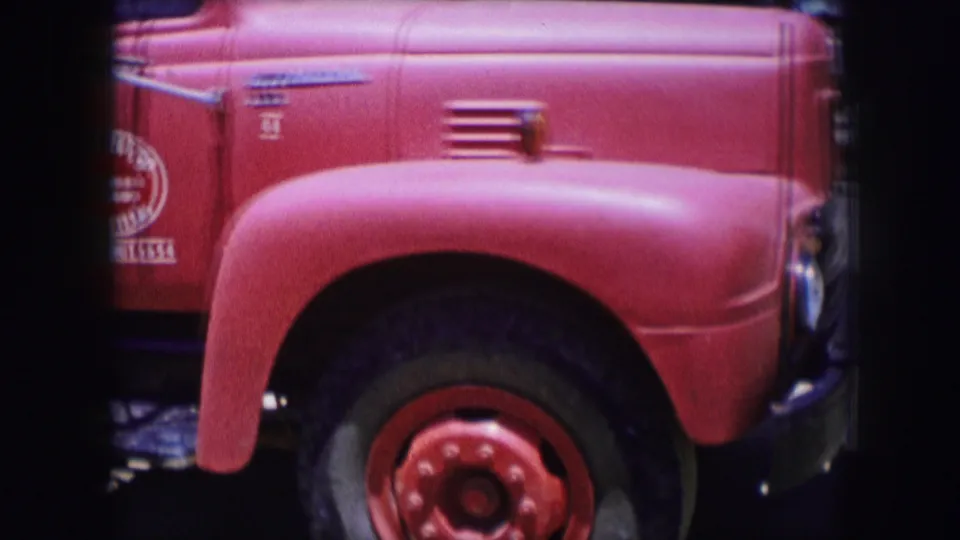 Close 8mm view of the red truck's hood, front fender, wheel, side vent, and partial service lettering in the Dallas 1964 footage.