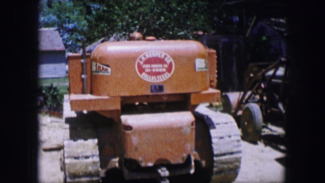 1964 Dallas 8mm frame showing an orange tracked tractor-like machine parked in a sunny yard, with a red circular logo visible.