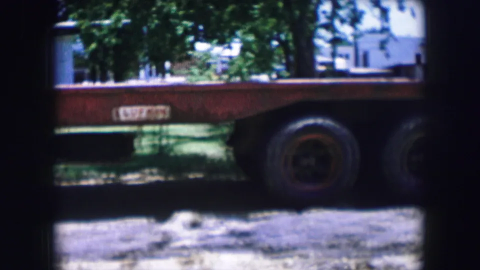 The final frame centers on the red flatbed trailer and its wheels, with trees and pale buildings beyond the yard.