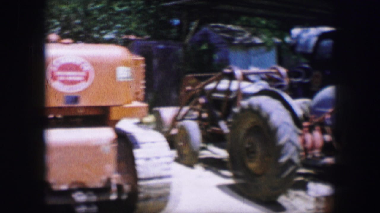 Orange tracked tractor parked outdoors beside other machinery in bright sun.
