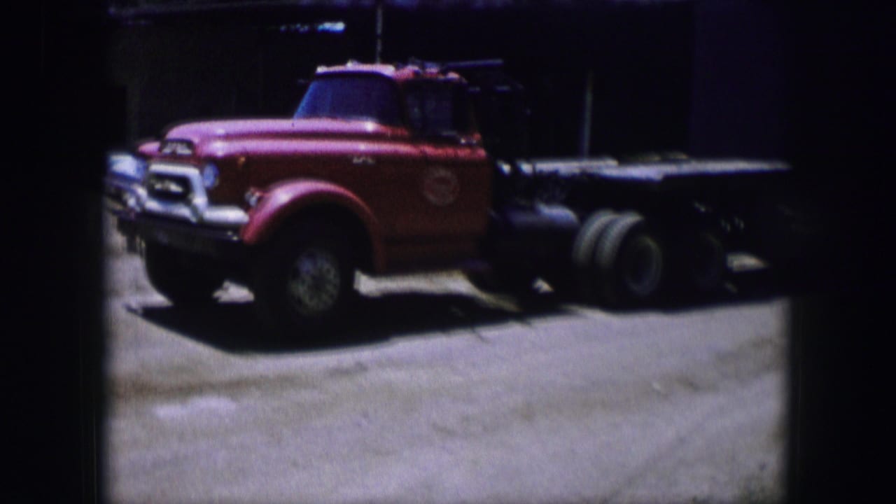 Red flatbed truck parked on pavement beside a dark building opening.