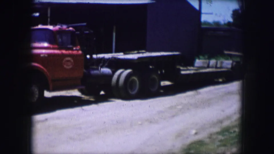 1964 Dallas 8mm frame showing the red flatbed truck farther right in frame, with its long bed, rear tires, and shaded background visible.
