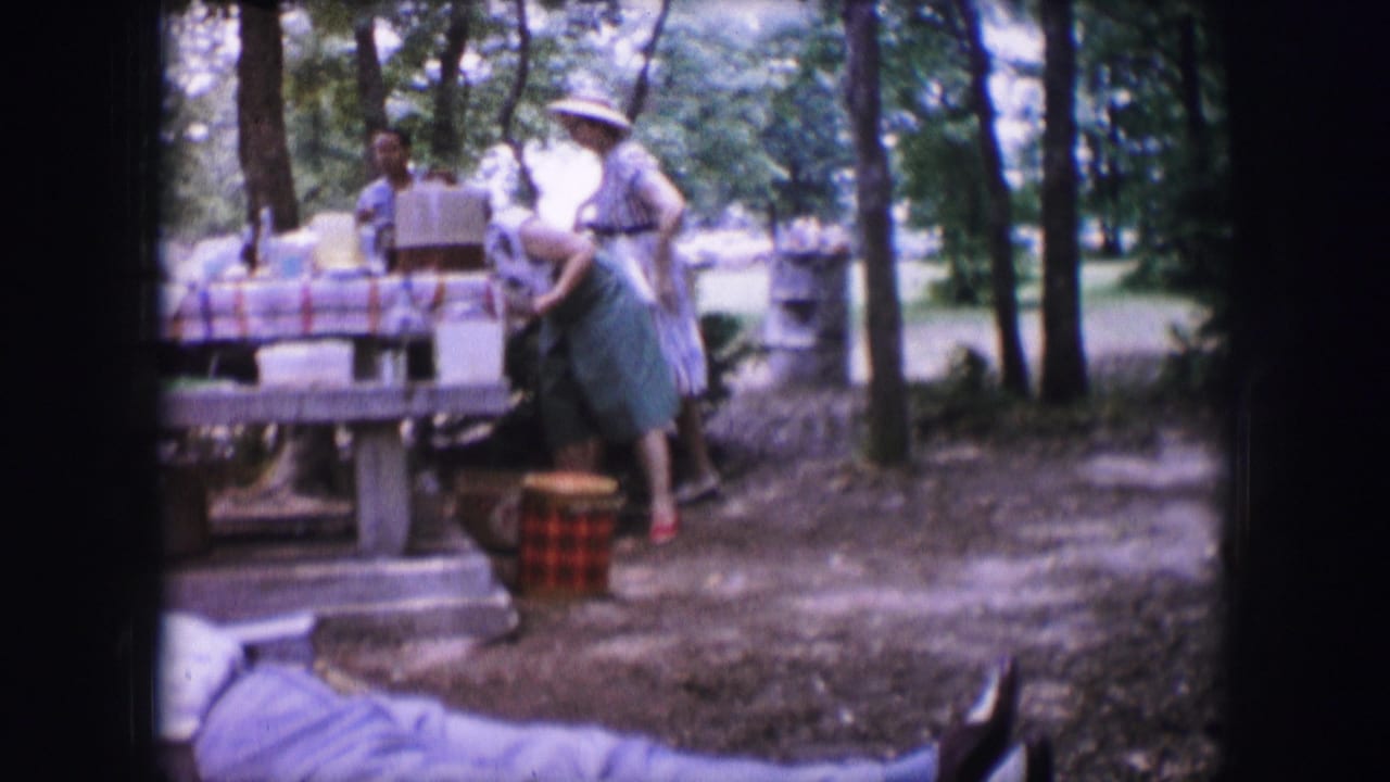 Woman in a green skirt bends near a red checked basket beside a picnic table.