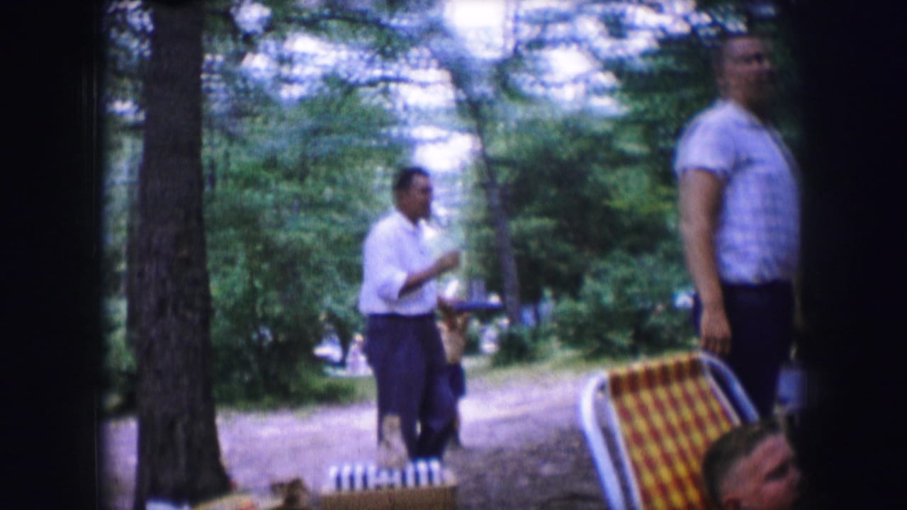 Two adult men near picnic seating, one carrying a plate in a wooded park.