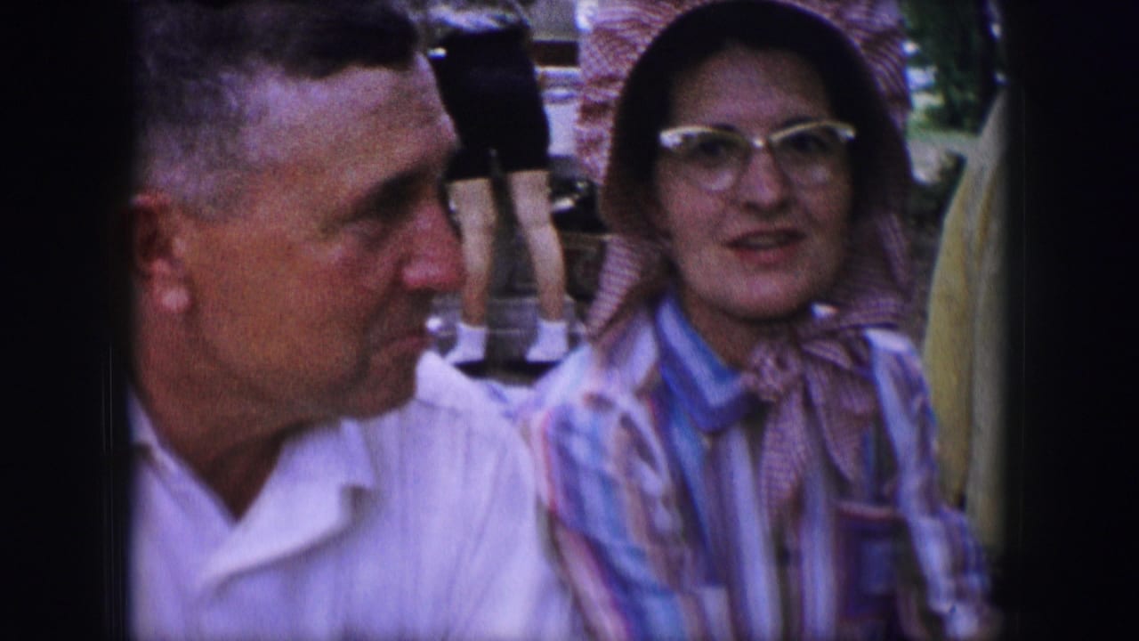 Man in a white shirt turns toward a woman in a bonnet and glasses.