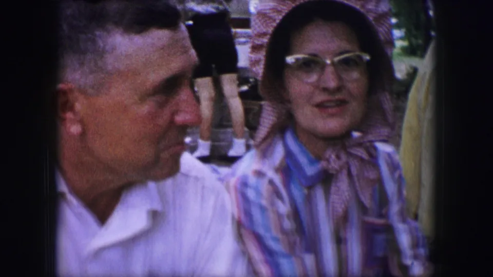 In the Dallas 1964 footage, a man in a white shirt faces a woman wearing a pink bonnet, glasses, and a striped blouse.