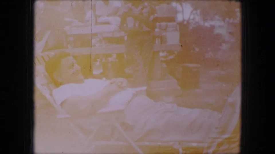 Soft, faded Dallas 1964 outdoor frame showing a man resting in a folding chair near adults gathered around picnic tables.
