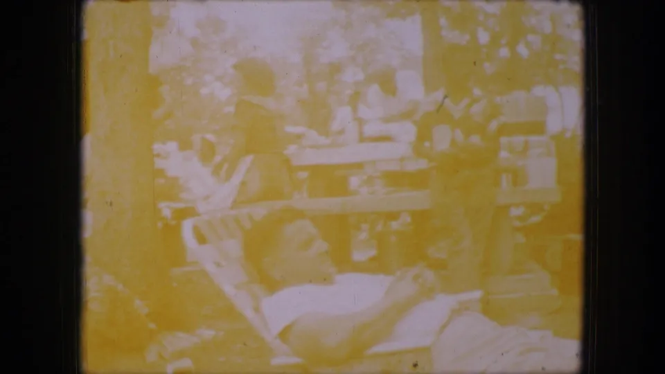 Dallas, Texas 1964 home-movie still with adults at picnic tables and a reclining man in the foreground under trees.