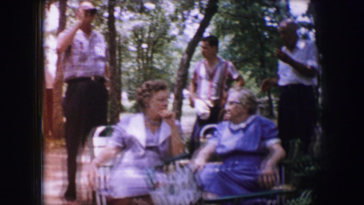 Dallas, Texas 1964 home-movie frame of two older women seated outdoors as several adults stand nearby under trees.