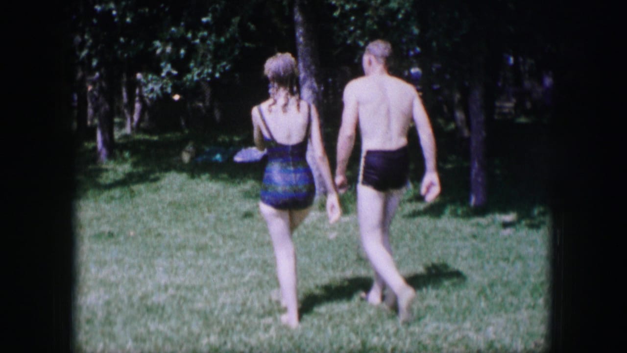 Couple in swimsuits walking across a sunny lawn toward trees.