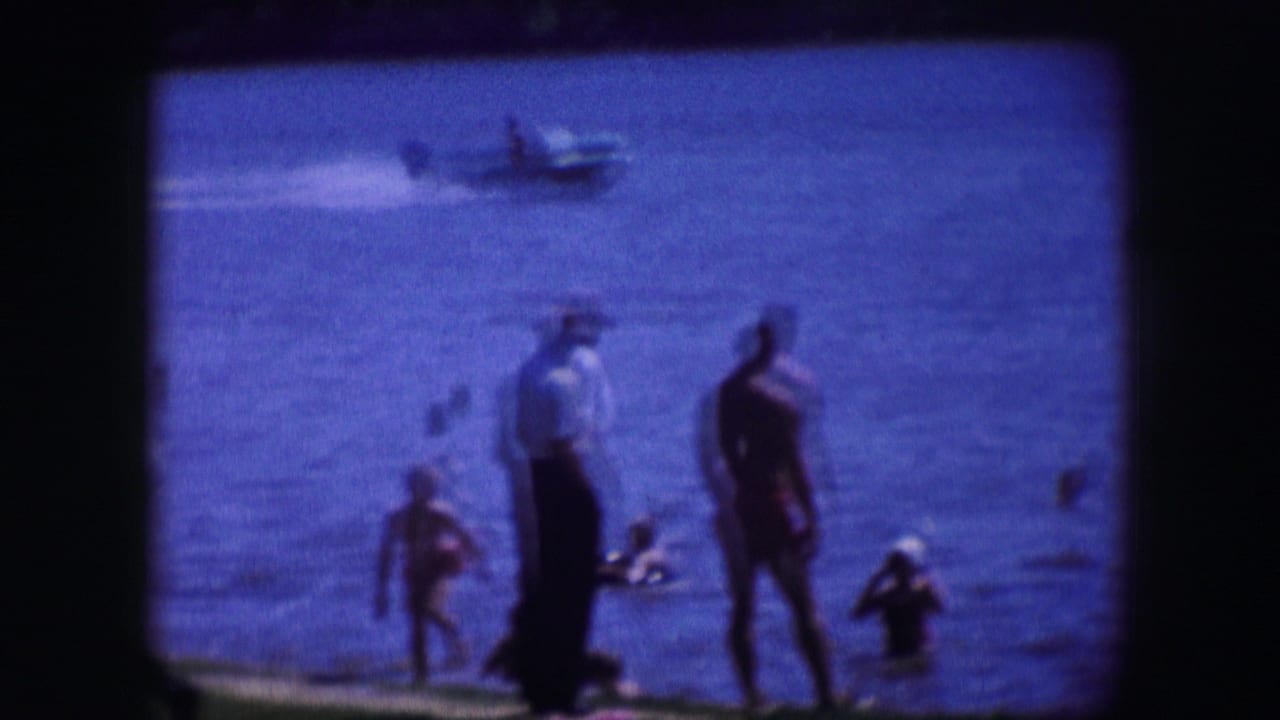 Swimmers and standing adults near blue water with a small boat in the distance.
