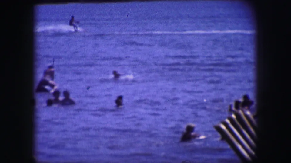 Swimmers are scattered across the water in the Dallas home-movie scene, with part of a dock or ladder visible at the right edge.