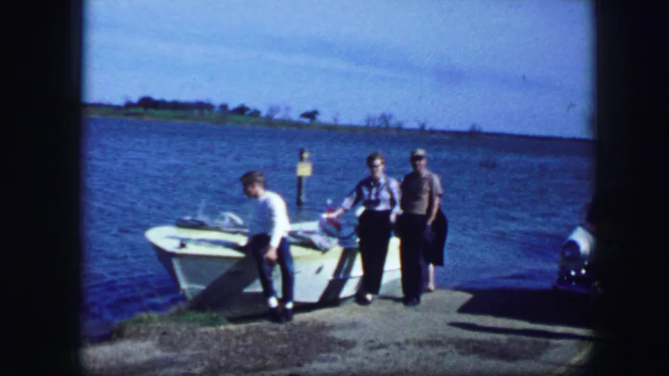 Lakeside 8mm frame from 1964 Fort Worth showing adults at a docked small boat with open water behind them.