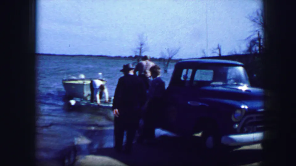 Several people gather by a blue pickup at a Fort Worth lakeside ramp, with a white boat partly in the water in 1964 footage.
