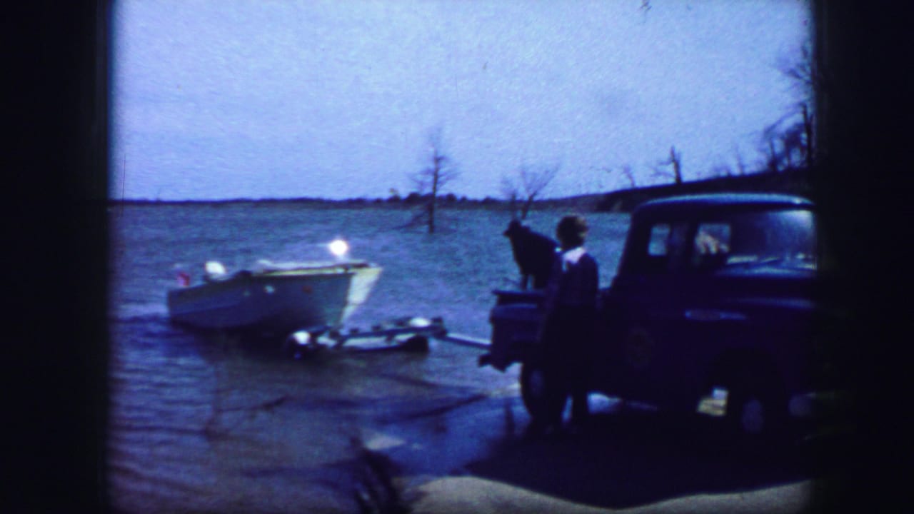 White boat in shallow water with a blue pickup and people near the shoreline.