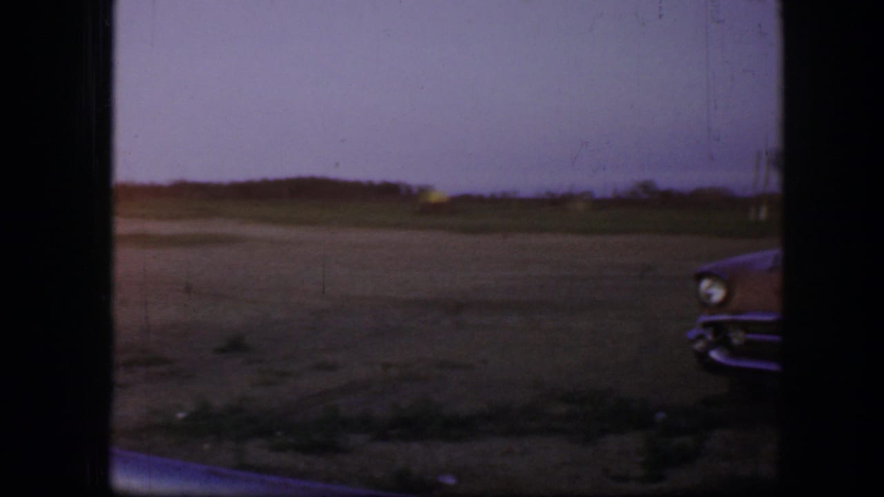 Open field at dusk with dark frame edges and a partial car front at right.