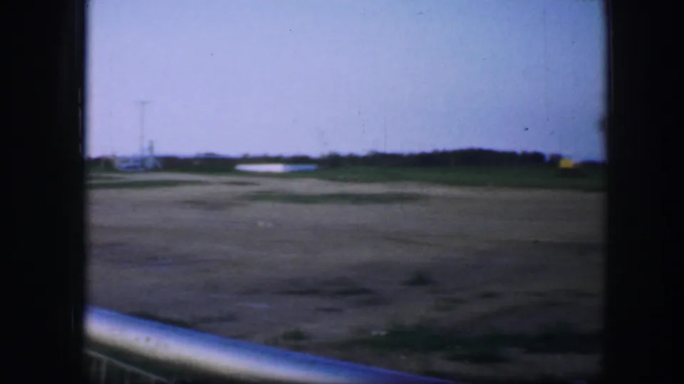 1964 Fort Worth frame with open ground, blue dusk sky, distant tree line, utility poles, and a pale railing crossing the lower foreground.