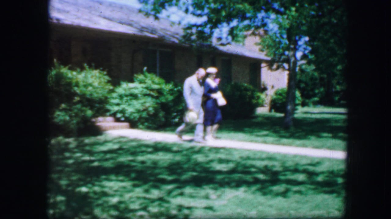 Adult couple walking arm-in-arm beside a lawn and brick residence.