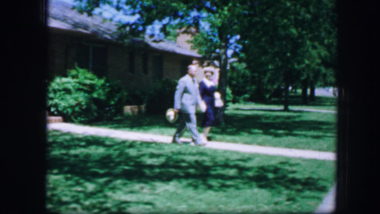Couple continuing along the sidewalk with trees and lawn behind them.