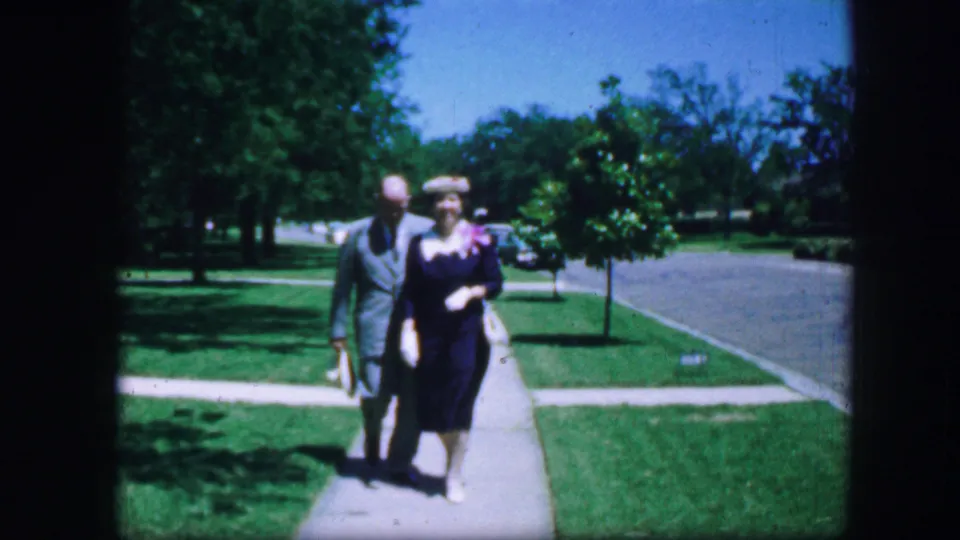 A formally dressed adult couple nears the camera on a sunny residential sidewalk in Fort Worth, Texas, according to clip metadata.