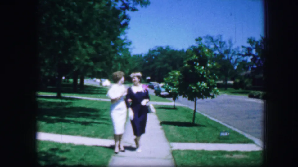 Two women walk arm-in-arm or close together toward the camera on a sunny Fort Worth sidewalk in 1964.
