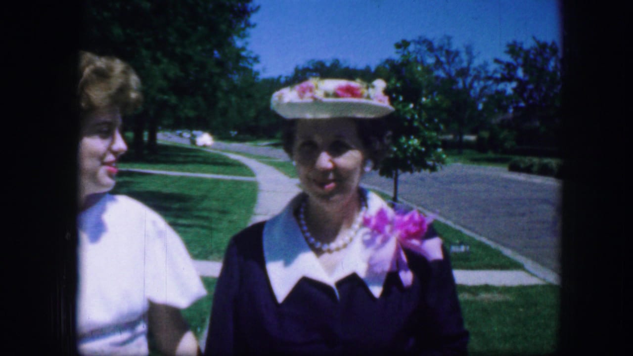 Two women in dress clothes stand close to the camera on a sunny sidewalk.